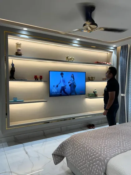 A large, custom-built TV and display unit in a master bedroom, complete with backlighting and gold accents.