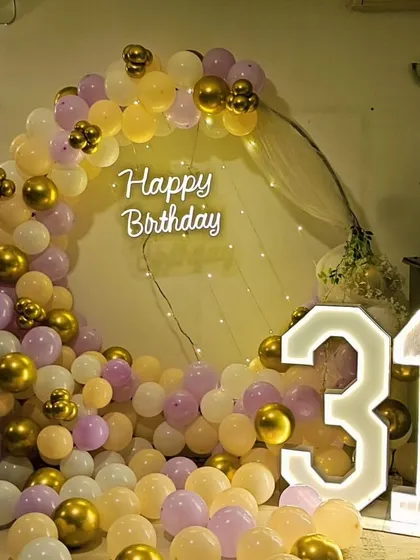A pretty pastel and gold 31st birthday. This setup features a half-arch of balloons with a neon sign and large light-up numbers.