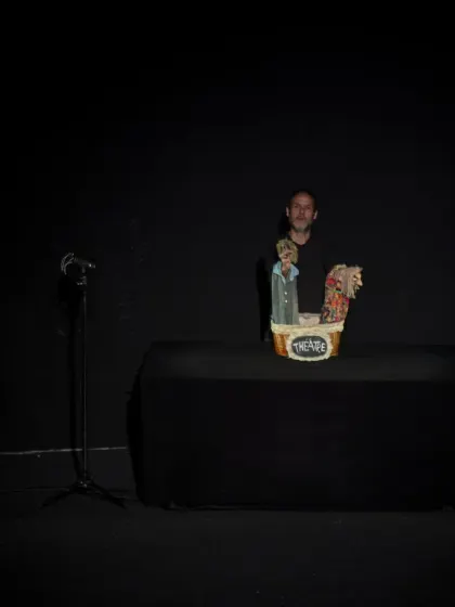 A wider view of the minimalist stage for 'Life (VIDA)'. The simple black box theatre focuses all attention on the puppeteer and the small basket of characters he brings to life.