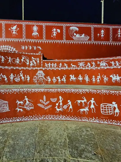 A close-up of the detailed Warli art, showing scenes of daily life, festivals, and nature painted along the curved steps.