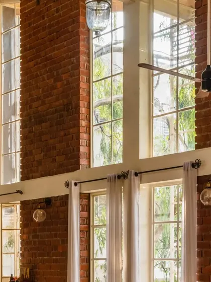 The double-height windows are a key feature of the loft, flooding the interior with sunlight and offering views of the surrounding greenery.