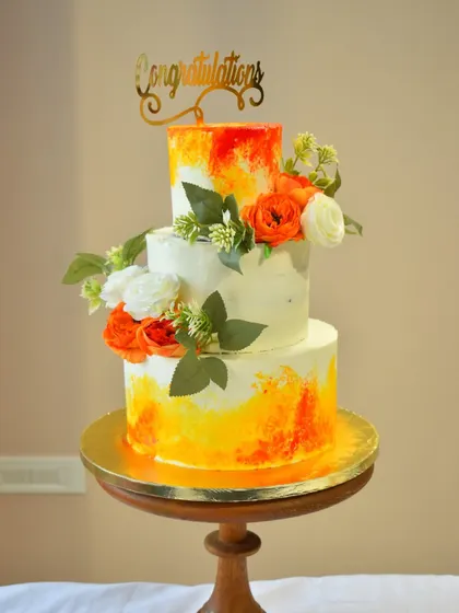 This three-tier cake uses a vibrant watercolor technique with sunset orange and yellow hues. Adorned with fresh flowers and a "Congratulations" topper, it's a bright and cheerful centerpiece for a wedding or engagement party.
