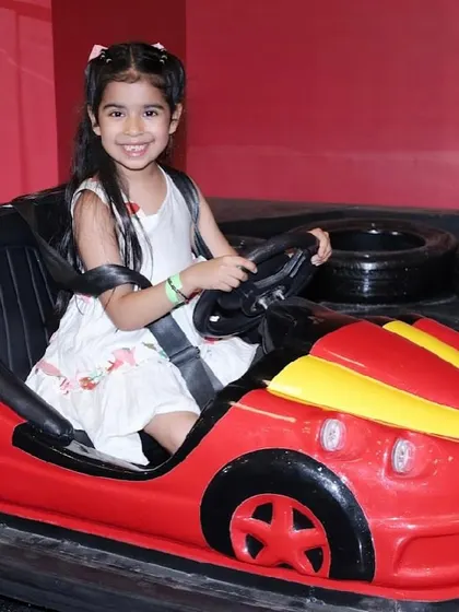 A smiling girl takes the wheel of her own bumper car, ready for a fun ride.