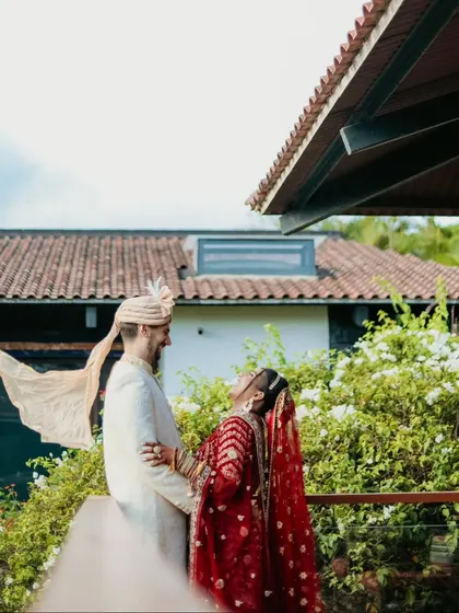 A playful, candid moment as the groom's "safa" blows in the wind, making the bride laugh.
