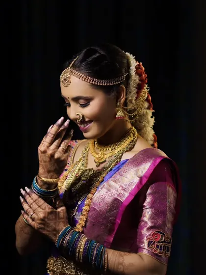 A candid portrait of a bride with a gentle smile, her hands framing her face, highlighting her intricate henna and jewelry.