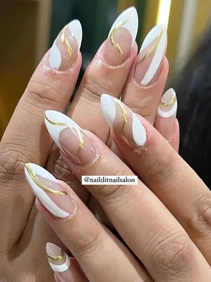 A classy and artistic design with white and gold abstract shapes on long almond nails. The use of negative space and clean lines creates a very modern and stylish look.