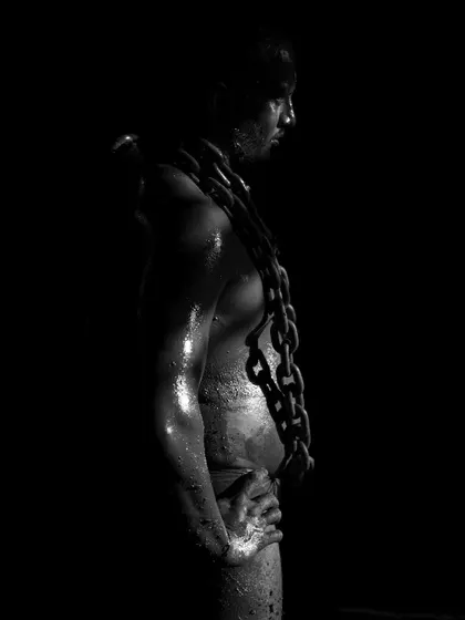 A series of dramatic, low-key portraits of a wrestler with heavy chains draped around his neck. These photos symbolize the immense strength and burden of the Pailwan's discipline.