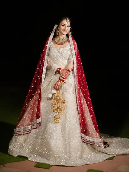 A full-length shot of the bride in her elegant white and red ensemble. She looks directly at the camera with a happy and confident smile, ready for her big day.