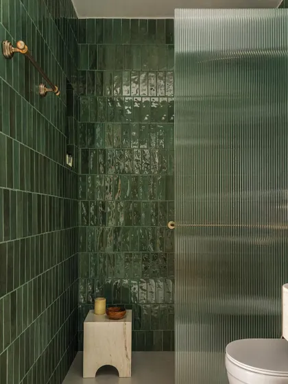 The bathroom in Apartment 1005 is a study in texture and color. We used handmade green ceramic tiles to create a rich, vibrant shower enclosure, contrasted with a fluted glass door that plays with light and transparency.