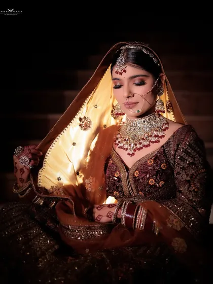 A beautiful close-up where the bride's dupatta casts a warm, golden glow on her face. This shot highlights her serene expression and the rich, heavy jewellery.