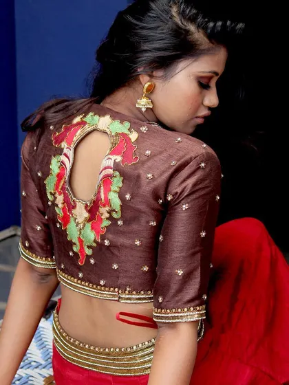 The back of a blouse is a canvas for creativity. This design features a unique keyhole back, framed by colorful floral embroidery on a rich brown raw silk fabric.
