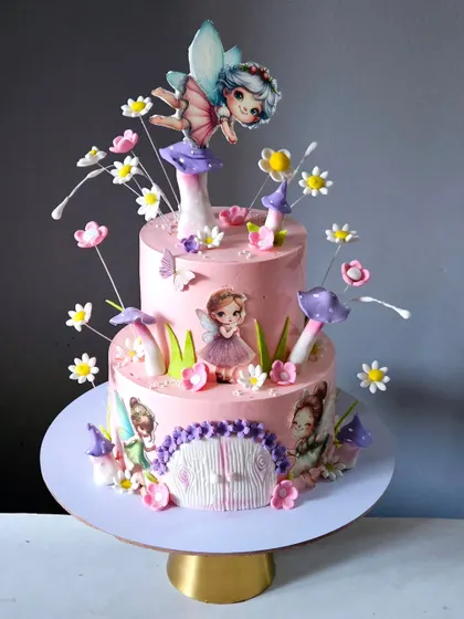 This two-tiered pink cake is a journey into a fairy-tale land. It is decorated with edible mushrooms, delicate sugar flowers, and printed fairy cutouts, with a larger fairy topper sitting on a mushroom.