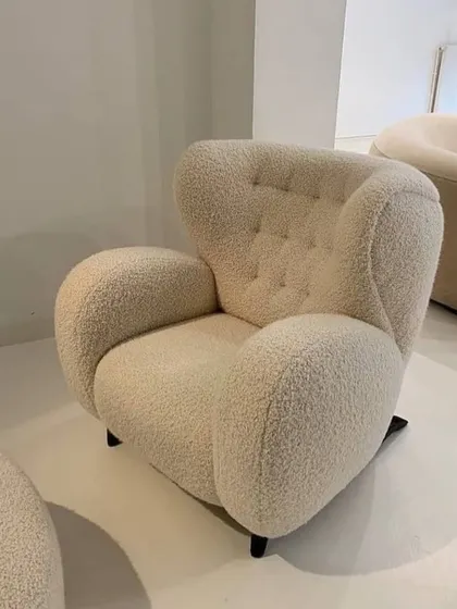 A modern, sculptural armchair upholstered in a cozy bouclé fabric. The rounded, organic shape and button-tufted back make it a comfortable and eye-catching accent piece.