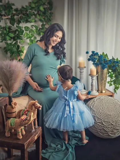 A whimsical moment between a mother-to-be and her toddler, who reaches out to touch her baby bump. The scene is set in a charming boho studio, adding to the magical feel.