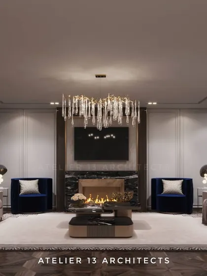 This formal living room is designed for symmetry and elegance, featuring a fireplace flanked by two bold blue armchairs. A cascading crystal chandelier and paneled walls add a layer of classic sophistication to the modern furnishings.