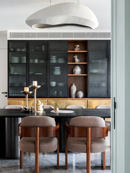 For me, a dining room is a stage for connection. Here, custom storage with fluted glass and brass shutters offers both style and function, while the sculptural pendant light casts a warm glow, creating a space that is both elegant and inviting for family gatherings.