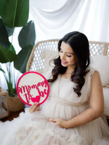 "Mommy to be." A sweet and simple announcement from this radiant mom-to-be, holding a sign in a beautiful, light-filled setting.