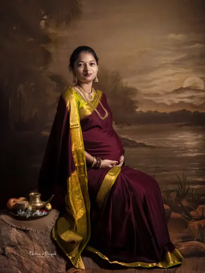 A fine-art portrait inspired by classic paintings. The mom-to-be in her saree looks serene and timeless against the painted landscape backdrop.