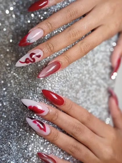 Slay your day with these fierce red and black nails, featuring hand-painted snakes and lips for a bold, edgy vibe.