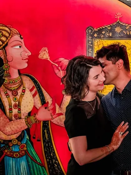 A romantic portrait of a cross-cultural couple against a vibrant, artistic wall mural, blending modern love with traditional art.