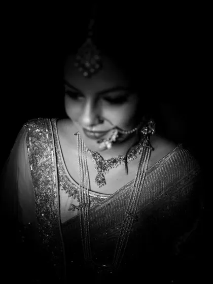 A classic black and white bridal portrait. The low-key lighting emphasizes the intricate details of her jewelry and the serene expression on her face, creating a timeless and elegant look.