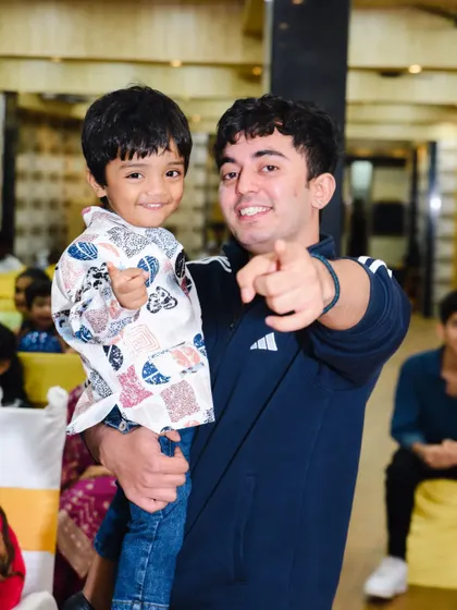 A candid shot of two boys sharing a smile and pointing at the camera during a birthday party.