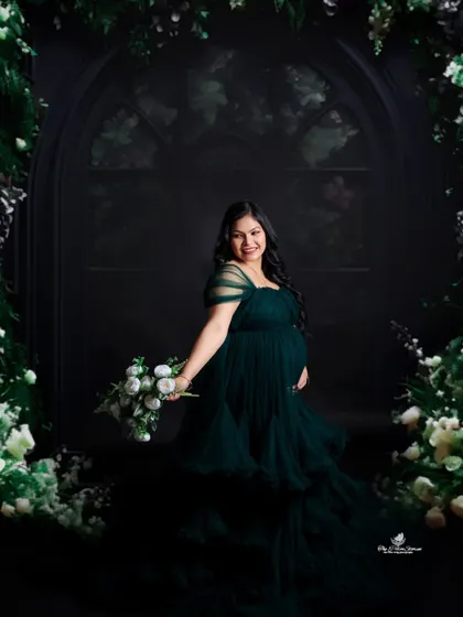An enchanting solo portrait. The mom-to-be holds a bouquet, framed by a dark floral arch that creates a moody, fairytale-like atmosphere.