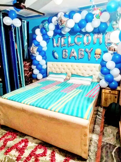 This bedroom is decorated to welcome a baby boy, featuring a blue and white balloon arch and rose petals on the floor spelling 'BABY'.