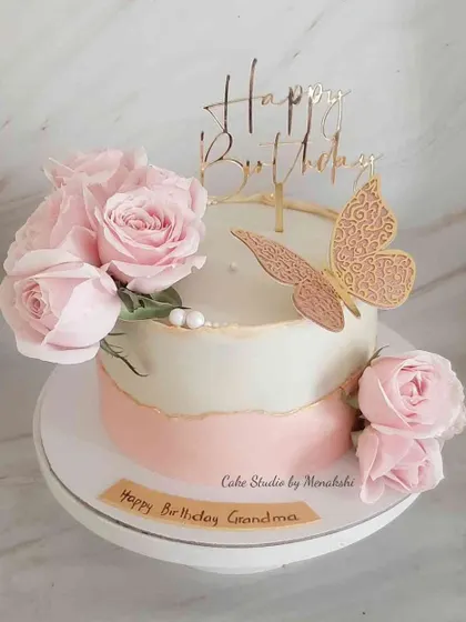 A beautiful and classic floral cake for a grandma's birthday. This no-fondant design has a soft pink ombre effect and is adorned with fresh pink roses and a golden butterfly.