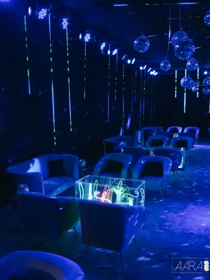 A vibrant and energetic after-party scene. The decor features neon lights, disco balls, and modern lounge furniture, creating a wild and unforgettable atmosphere.