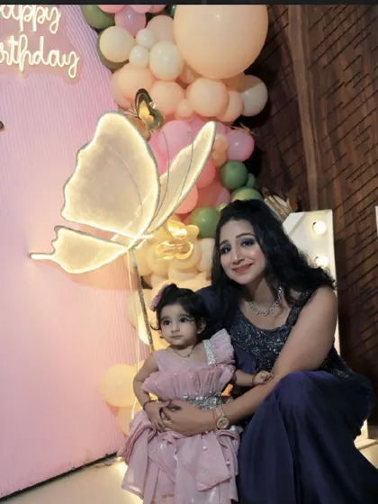 A mother and daughter share a sweet moment in front of a butterfly-themed birthday setup, featuring a neon butterfly light.