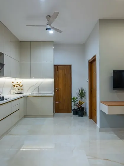 This view shows the L-shaped kitchen layout and its proximity to the dining and TV area. The consistent flooring and neutral wall colors create a cohesive flow between the different zones.