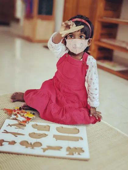 A child proudly holds up a piece from a wooden puzzle. Puzzles like these help develop problem-solving skills, shape recognition, and fine motor control.