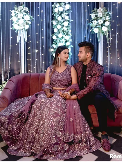 A lovely portrait of the couple seated on a sofa at their engagement party, set against a backdrop of fairy lights and flowers.
