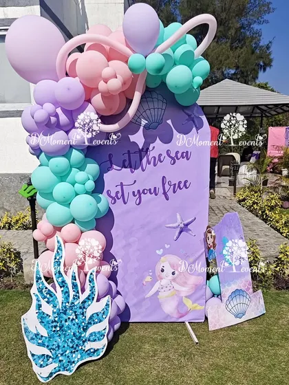 A simple yet beautiful photo prop for an outdoor mermaid party, with a "Let the sea set you free" message and a pastel balloon garland.