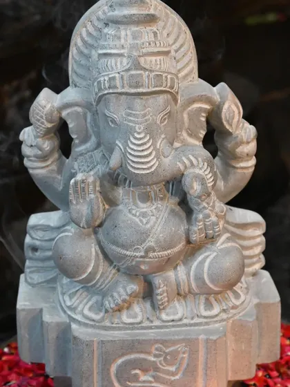 A stone Ganesha statue surrounded by incense smoke, creating a spiritual ambiance. This piece is a product of 'Kai kelasa', or handwork, a skill that allows our artisans to reveal the divine from natural stone.