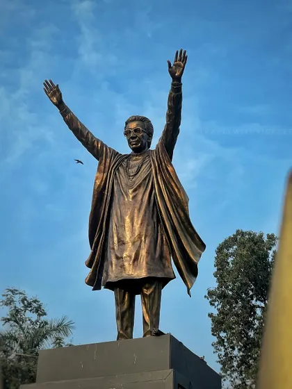 A close-up shot of the Balasaheb Thackeray statue, with a bird flying past, capturing a moment of stillness.