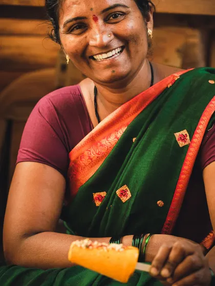 A joyful portrait of a woman holding a mango popsicle, her bright smile reflecting the sweetness of the treat.