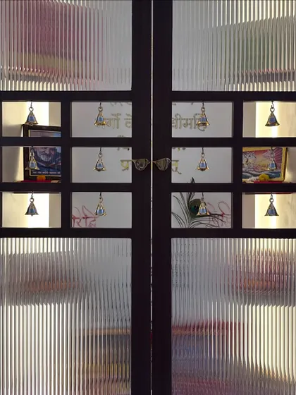 A full view of the double doors for the pooja room, showcasing the intricate design with fluted glass and multiple niches for bells, blending privacy with a sense of openness.