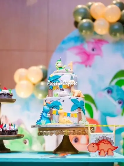 The beautiful dinosaur-themed cake and cupcakes. The cake is decorated with little dinos and palm trees, perfectly matching the backdrop.