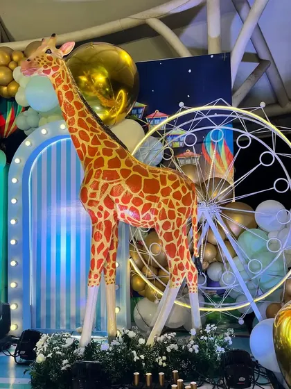 A life-size giraffe prop next to a neon-lit Ferris wheel, adding a touch of magic to the circus theme.