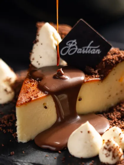 A close-up of the iconic Bastian cheesecake. We focused on capturing the rich, molten chocolate pour over the creamy texture of the cake and the crumble, creating a dark, moody, and decadent shot that emphasizes indulgence.
