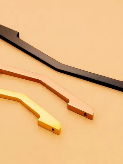 Three elegantly curved handles in different metallic finishes. The minimalist composition emphasizes their unique shape and form.