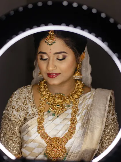 A close-up of the bride, framed by a ring light. Her makeup is flawless, and her white and gold saree looks ethereal.