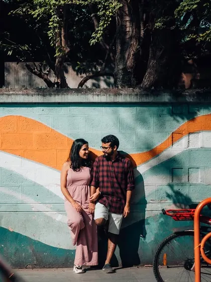 A couple stands against a colorful mural, their casual poses reflecting a relaxed and modern pre-wedding vibe.