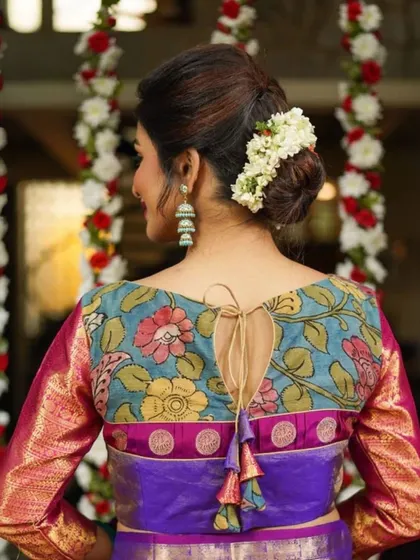 The back of this blouse is a masterpiece, featuring a keyhole opening and a tie-up tassel, framed by beautiful Kalamkari floral art.
