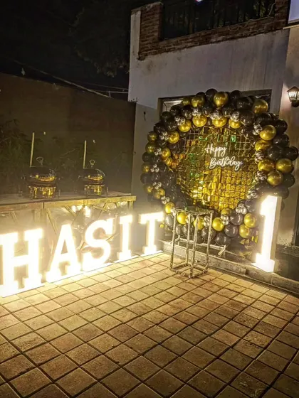 The combination of the gold and black balloon ring and the large light-up letters creates a grand statement for an outdoor party.