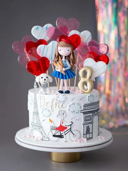 An "Emily in Paris" themed cake for an 8th birthday. This cake is decorated with hand-drawn Parisian landmarks and heart-shaped lollipops.