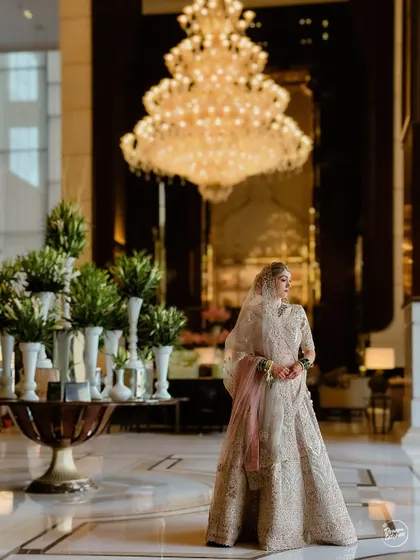 A wide shot of the bride in the grand lobby of the Ritz-Carlton, her elegant lehenga contrasting beautifully with the opulent surroundings.