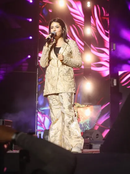 A full-body shot of Hargun Kaur performing, showing her stylish outfit against the vibrant stage background. I provide comprehensive coverage that includes artist styling and stage design.